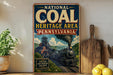 A vintage-style metal sign for the National Coal Heritage Area in Pennsylvania, featuring an illustration of a coal train and a scenic landscape.