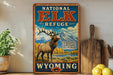 A vintage-style sign for the National Elk Refuge in Wyoming, featuring an illustration of a majestic elk standing in a scenic landscape with mountains in the background.