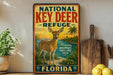 A vintage-style sign for the National Key Deer Refuge in Florida, featuring an illustration of a deer in a tropical setting.