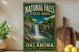 A vintage-style sign for Natural Falls State Park in Oklahoma, featuring a waterfall and lush greenery, is displayed on a shelf next to a wooden cutting board and some lemons.
