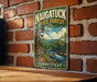 A vintage-style metal sign for the Naugatuck State Forest in Connecticut, featuring a scenic image of a forest and a river.