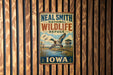 A vintage-style metal sign for the Neal Smith National Wildlife Refuge in Iowa, featuring a duck flying over a body of water and a small building in the background.