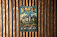 A vintage metal sign for the Nemacolin Castle in Pennsylvania, featuring an illustration of the castle and the text "A DESTINATION LIKE NO OTHER PENNSYLVANIA HISTORY LUXURY MEMORIES".
