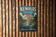 A vintage metal sign for Nemours Estate in Delaware, featuring an illustration of a grand mansion surrounded by lush gardens and a fountain.
