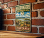 A vintage-style metal sign displaying the name "NGORONGORO CONSERVATION AREA" and the word "TANZANIA" is hanging on a brick wall.
