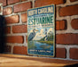 A vintage-style metal sign for the North Carolina Estuarine Research Reserve, featuring a lighthouse and a bird, is displayed on a brick wall.