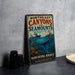 A vintage-style sign for the Northeast Canyons and Seamounts, featuring an illustration of a ship and marine life, is displayed on a gray countertop next to a stack of black camera lenses.