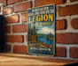 A vintage-style metal sign for the Northern Highland American Legion State Forest in Wisconsin, featuring a scenic illustration of a lake surrounded by pine trees and mountains.