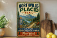 A vintage-style sign for Northville-Placid Trail, featuring a scenic mountain landscape and trail marker, is displayed on a shelf next to a wooden cutting board and some lemons.
