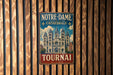 A vintage metal sign with the text "NOTRE-DAME CATEDRALE TOURNAI BELGIQUE" hanging on a wooden wall.