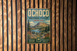 A vintage metal sign for Ochoco National Forest in Oregon, featuring a scenic landscape with mountains, forests, and a river.