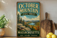 A vintage-style metal sign for October Mountain State Forest in Massachusetts, featuring a scenic landscape with mountains, forests, and a river.