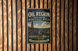 A vintage-style metal sign for the Pennsylvania Oil Region National Heritage Area, featuring an illustration of a town and a steam tower.