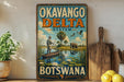a vintage-style sign for the Okavango Delta System in Botswana, with a painting of a man in a boat on a river surrounded by wildlife.