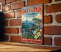 A vintage-style metal sign for "OKI ISLANDS PARK JAPAN" is displayed on a brick wall, featuring a scenic landscape with mountains, water, and flowers.