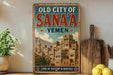 a vintage-style sign for the "Old City of Sana'a" in Yemen, with a picture of a cityscape and text indicating it is a "Land of History & Heritage".