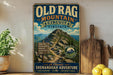 a vintage-style sign for the Old Rag Mountain Circuit in Virginia, with a mountain landscape and trail sign. The sign is displayed on a shelf next to a wooden cutting board and a potted plant.