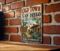 A vintage-style metal sign for Old Town San Diego, California, featuring a brick wall and a sign with a welcoming message.