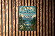 A vintage-style metal sign for the Olympic National Forest in Washington, featuring a scenic mountain landscape with pine trees, a river, and flowers.