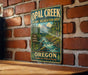 A vintage metal sign for Opal Creek Scenic Recreation Area in Oregon, featuring a scenic mountain landscape with a flowing river.