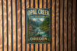 A vintage metal sign for Opal Creek Scenic Recreation Area in Oregon, featuring a scenic mountain landscape with a flowing river.