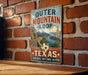 A vintage-style metal sign with the text "Outer Mountain Loop" and "Texas" is displayed on a brick wall.