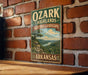 A vintage-style metal sign with the text "OZARK HIGHLANDS HERITAGE LANDSCAPE ARKANSAS" is displayed on a brick wall.