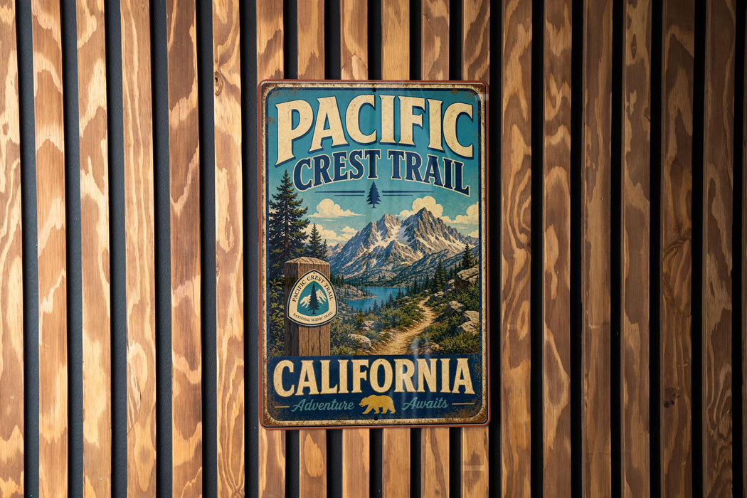 A vintage metal sign for the Pacific Crest Trail in California, featuring a scenic mountain landscape and a path leading to a lake.
