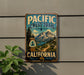 A vintage-style metal sign for the Pacific Crest Trail in California, featuring a scenic mountain landscape and a trail marker.