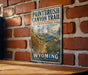 A vintage-style sign for the Paintbrush Canyon Trail in Grand Teton National Park, with a mountain landscape and a path leading through the scene.