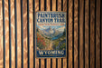 A vintage-style metal sign for the Paintbrush Canyon Trail in Grand Teton National Park, with a mountain landscape and text indicating the trail's name.