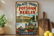 A vintage-style metal sign displaying the text "Palaces and Parks of Potsdam and Berlin" along with an illustration of the city's landmarks, including the Brandenburg Gate and the Brandenburg Palace.
