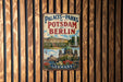 A vintage metal sign displaying the text "Palaces of Potsdam and Berlin" and "GERMANY" against a backdrop of a wooden fence.
