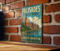 A vintage metal sign for Palisades State Park in South Dakota, featuring a scenic mountain landscape with a lake in the background.