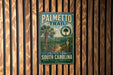 A metal sign with a tropical landscape and trail information is mounted on a wooden wall.