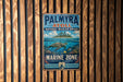 A metal sign with a tropical island scene and a sea turtle, mounted on a wooden wall.