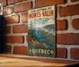 A vintage metal sign for the Park National des Monts-Valin in Quebec, featuring a scenic mountain landscape with a river and pine trees.