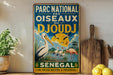 A vintage-style metal sign with text and illustrations, including a large bird, is displayed on a shelf next to a wooden cutting board and some fruit.