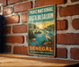 A vintage-style metal sign with a tropical scene, featuring a bird, palm tree, and a sunset over a body of water.