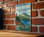 A vintage-style metal sign with a mountain landscape and a lake, mounted on a brick wall.