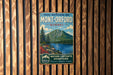 A vintage metal sign with a mountain landscape and a lake, mounted on a wooden wall.