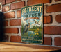 A vintage-style metal sign with the text "Patuxent Research Refuge Maryland" and an illustration of a bird and a pond, mounted on a brick wall.