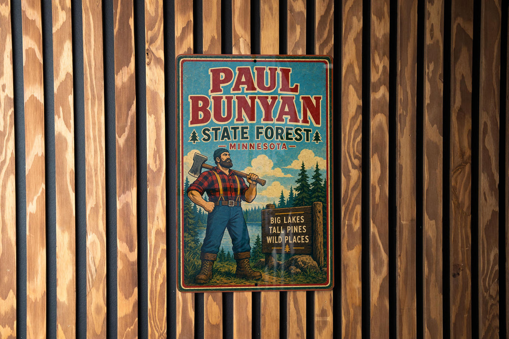 A vintage Paul Bunyan sign advertising a state forest in Minnesota, featuring a woodcut illustration of a lumberjack holding a chainsaw and standing in front of a sign that reads "Big Lakes Tall Pines Wildplains".