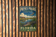 A vintage metal sign for Paynes Prairie Preserve State Park in Florida, featuring an illustration of a horse, alligator, and bird in a grassy field with a river.