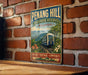 A vintage-style metal sign with a train and tropical landscape, mounted on a brick wall.