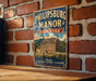 A vintage-style metal sign for "Philipsburg Manor" in New York, featuring an illustration of a historic house and a banner that reads "A NATIONAL HISTORIC LANDSCAPE EXPERIENCE 500 YEARS OF HISTORY".