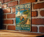 A vintage-style metal sign for the Pictured Rocks Lakeside Trail in Michigan, featuring a scenic image of a cliff overlooking a lake.