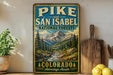 A vintage-style sign for the Pikes and San Isabel National Forests in Colorado, featuring a scenic mountain landscape with pine trees and a river.