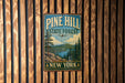 A vintage-style metal sign for Pine Hill State Forest in New York, featuring a scenic landscape with pine trees, mountains, and a lake.