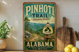 A vintage-style sign for the Pinedoni Trail in Alabama, featuring a scenic mountain landscape and the trail's name.